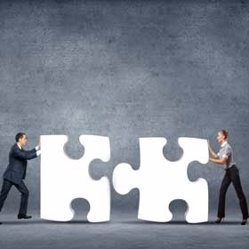 A man and a woman each pushing a large white puzzle piece towards each other