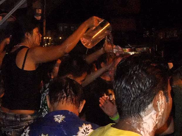 Night scene at Songkran: a woman pours a jug of water over the heads of the crowd