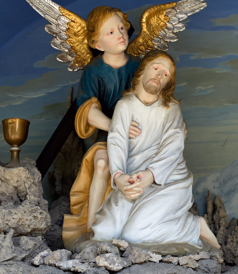 Painted statue of Jesus kneeling in prayer with an angel behind him and a golden chalice beside them