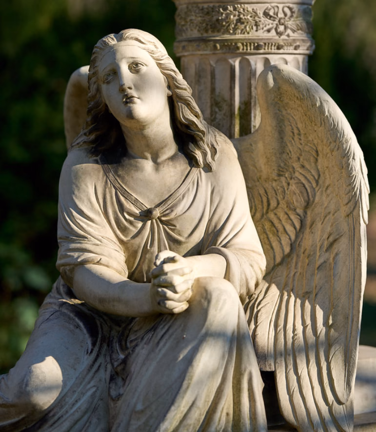 Stone angel statue sitting with folded hands and looking upwards, a column behind her