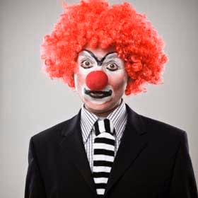 Person in clown wig and red nose wearing a black suit and striped tie
